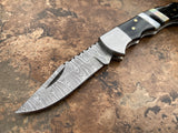 Ebony Tide Buffalo Horn and Mother of Pearl folding knife's Damascus steel clip point blade on a textured surface