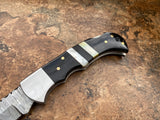 Ebony Tide Buffalo Horn and Mother of Pearl folding knife's handle on a textured brown surface