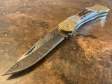 Handcrafted Damascus steel engraved bolster folding pocket knife with a detailed blade on a textured surface