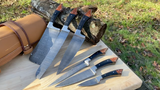 Set of 6 Piece Damascus steel kitchen chef knives with leather sheath on a wooden surface outdoors