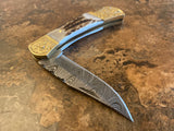 Handmade Damascus Steel Engraved Bolster folding knife with decorative blade and gold-colored handle on a textured surface