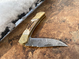 Foldable knife with Damascus steel blade and a stag handle on a textured surface