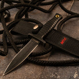 MTech USA MT-097 fixed blade boot knife with a black double-edged spear point blade and ribbed black rubber handle, resting on a dark surface next to its black nylon sheath and tactical rope.