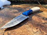 Damascus knife with a camel bone handle and sapphire blue bolster on a textured surface