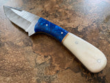 Damascus knife with a camel bone handle, Damascus steel blade, and sapphire blue acrylic bolster on a textured surface