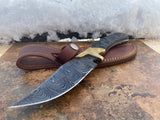 Obsidian Hunter Custom Tactical knife with a damascus steel blade and leather sheath on a stone surface with snow in the background