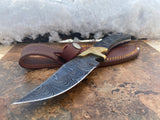 Obsidian Hunter knife with a Damascus steel blade and brown sheath on a stone surface with snow in the background