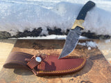 Obsidian Hunter Custom Tactical knife with a damascus steel blade, black micarta handle, and leather sheath on a stone surface with snow in the background