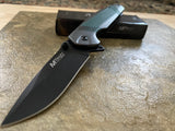 Folding knife with black blade and silver handle on a textured surface