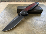 Folding knife with red accents on a stone surface, next to its black box.